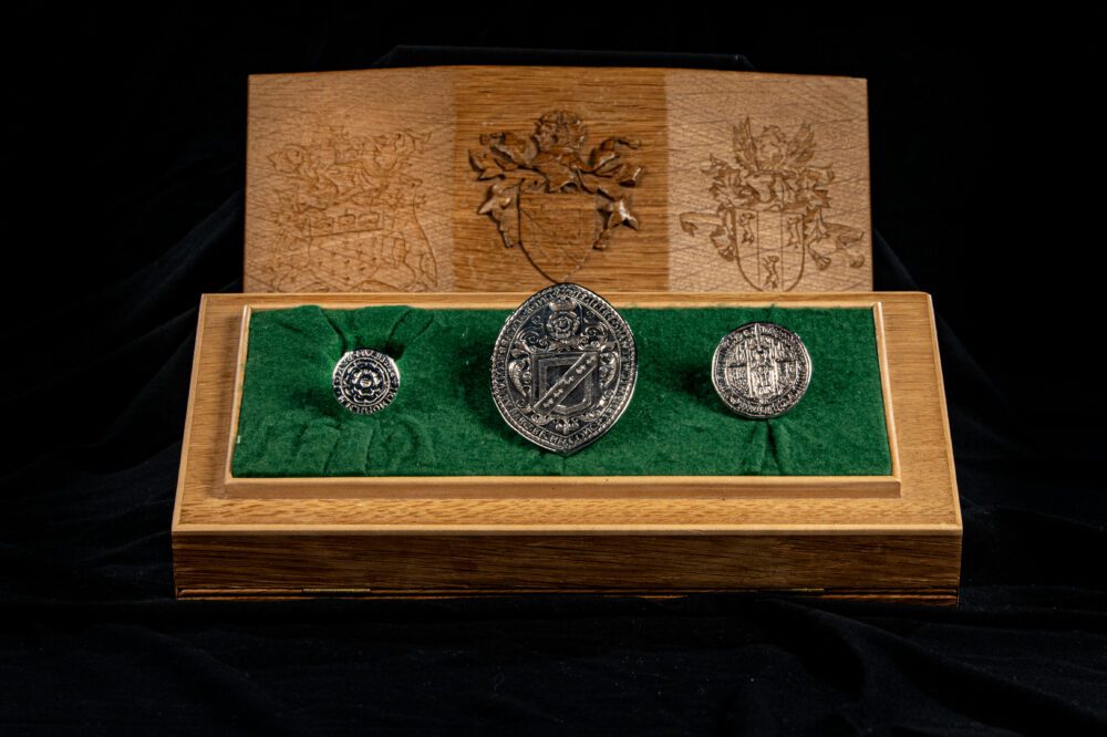 Three silver seals placed on a green inlay inside a small oak box, with decorative etchings.